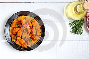 Baked pumpkin pieces with spices and herbs on white wooden background. Diet menu. Vegetarian dish. The top view