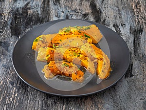 Baked pumpkin slices with aromatic herbs on a black plate