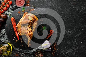 Baked quail, chicken with chili pepper on a black stone plate. Top view,