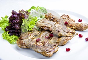 Baked quails with greens on a white plate