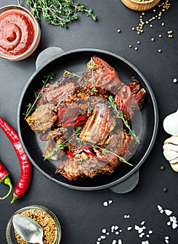 Baked ribs in a pan. Roasted ribs with spices and herbs on a dark background. Food background. View from above. Copy space