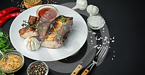 Baked ribs on a plate. Roasted ribs with spices and herbs on a dark background. Food background. Side view. Banner. Copy space
