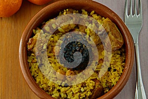 Baked rice in a pottery dish accompanied by pork, chickpeas, blood sausage, tomato and garlic. Traditional photo