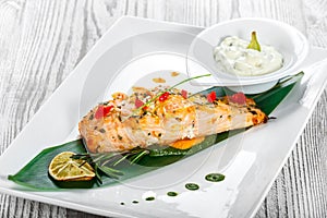 Baked salmon with cheese sauce, rosemary and lemon on wooden background. Hot fish dish.