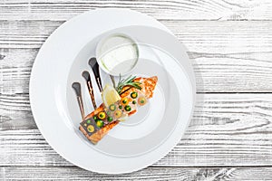 Baked salmon with cheese sauce, rosemary and lemon on wooden background close up