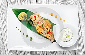 Baked salmon with cheese sauce, rosemary and lemon on wooden background. Hot fish dish.