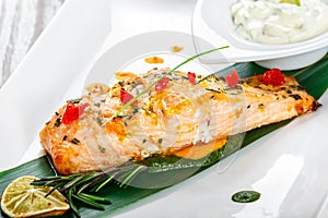 Baked salmon with cheese sauce, rosemary and lemon on wooden background. Hot fish dish.