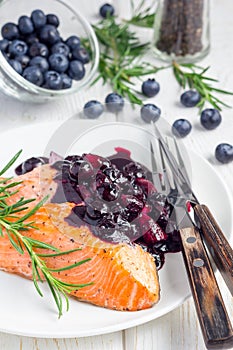 Baked salmon fillet with blueberry rosmarin sauce on white plate