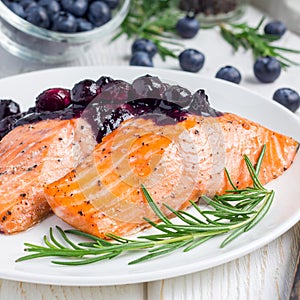 Baked salmon fillet with blueberry and rosmarin sauce on white plate, square