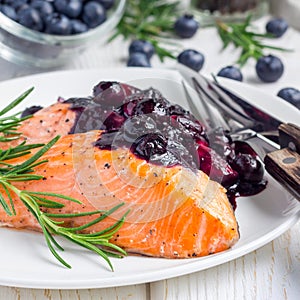 Baked salmon fillet with blueberry and rosmarin sauce on white plate, square format