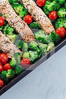 Baked salmon fillet with broccoli and tomato on frying tray, vertical, top view