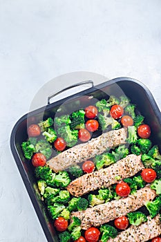 Baked salmon fillet with broccoli and tomato on frying tray, vertical, top view, copy space