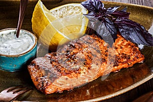 Baked salmon fillet with cheese sauce, basil and lemon on plate on wooden background.