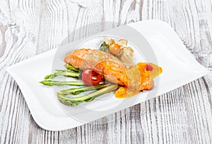 Baked salmon garnished with physalis, asparagus, tomatoes with herbs on wooden background.