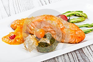 Baked salmon garnished with physalis, asparagus, tomatoes with herbs on wooden background.