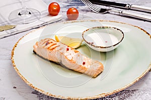 Baked Salmon Steak with herbs, sauce and lemon slice on plate. Delicious fried fish served coarse salt and cherry tomato branch