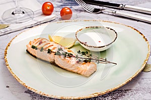 Baked Salmon Steak with herbs, sauce and lemon slice on plate. Delicious fried fish served coarse salt and cherry tomato branch