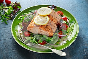Baked salmon steak with tomato, onion, mix of green leaves salad in a plate. healthy food