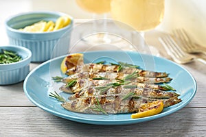 Baked sardines with rosemary and lemon in a blue bowl, two glasses of white wine