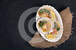 Baked scallops with caviar and creamy garlic sauce in white plate. Scallops with lemon on black background with napkin. Top view.