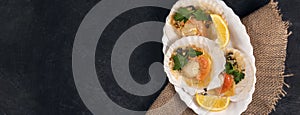 Baked scallops with caviar and creamy garlic sauce in white plate. Scallops with lemon on black background with napkin. Top view.