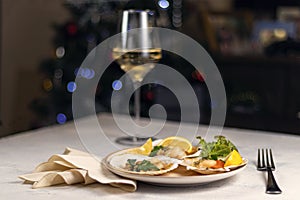 Baked scallops with caviar in a plate against the background of blurred glasses of wine. Scallops with lemon on a black background