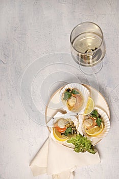 Baked scallops with caviar in a plate and glass of white wine. Scallops with lemon on a black background with a napkin and a fork