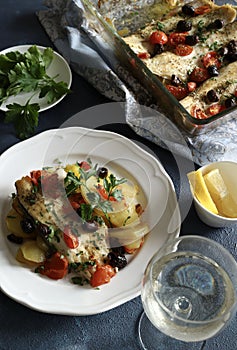Baked sea bass fillets with cherry tomatoes, olives and baked potato side dish.