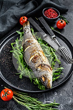 Baked sea Bass fish with arugula, grilled seabass. Black background. Top view