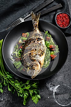 Baked sea bream fish with arugula salad and tomatoes. Black background. top view