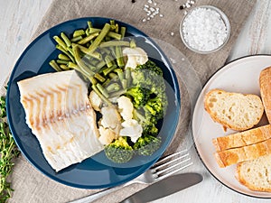 Baked sea fish cod fillet with vegetables on blue plate, bread,