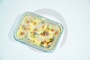 Baked spinach with cheese in aluminum tray on white background