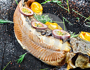 Baked sturgeon fish with rosemary, lemon and passion fruit on plate on wooden background close up.