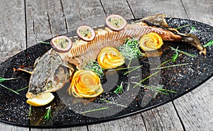 Baked sturgeon fish with rosemary, lemon and passion fruit on plate on wooden background close up.