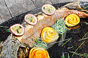 Baked sturgeon fish with rosemary, lemon and passion fruit on plate on wooden background close up.