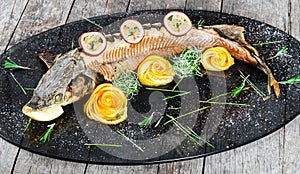 Baked sturgeon fish with rosemary, lemon and passion fruit on plate on wooden background close up.