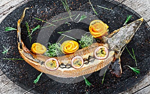 Baked sturgeon fish with rosemary, lemon and passion fruit on plate on wooden background close up