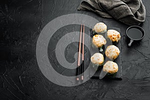 Baked sushi maki rolls with salmon, crab, cucumber, avocado, flying fish roe and spicy sauce, on black stone background , with