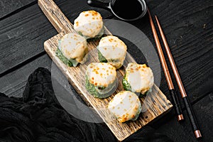 Baked sushi maki rolls with salmon, crab, cucumber, avocado, flying fish roe and spicy sauce, on black wooden table background