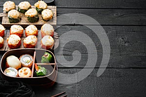 Baked sushi maki rolls with salmon, crab, cucumber, avocado, flying fish roe and spicy sauce, on black wooden table background ,