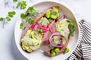 Baked sweet potato halves with guacamole, edamame beans, pickled red onion and cilantro