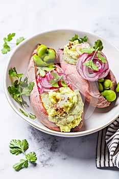 Baked sweet potato halves with guacamole, edamame beans, pickled red onion and cilantro