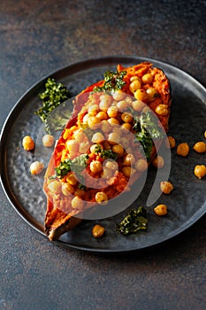 Baked sweet potato stuffed with chickpea and crunchy kale on a black plate
