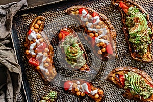 Baked sweet potato toast with roasted chickpeas, tomatoes, goat cheese, sauce guacamole, avocado, seedlings on baking tray over