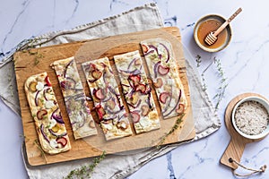 Baked tarte flambee with rhubarb, red onions, goat cheese and honey, cut into strips, marble background