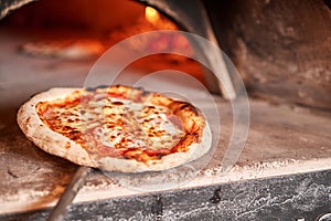 Baked tasty margherita pizza in Traditional wood oven in Naples restaurant, Italy. Original neapolitan pizza. Red hot photo