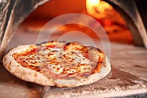 Baked tasty margherita pizza in Traditional wood oven in Naples restaurant, Italy. Original neapolitan pizza. Red hot