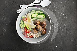 Baked teriyaki meatballs with brown rice, cucumbers, hot pepper, lemon slices in a bowl. Top View