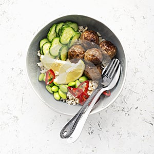 Baked teriyaki meatballs with brown rice, cucumbers, hot pepper, lemon slices in a bowl. Top View