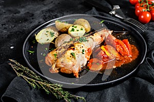 Baked in tomatoes monkfish with potatoes and vegetables. Black background. Top view